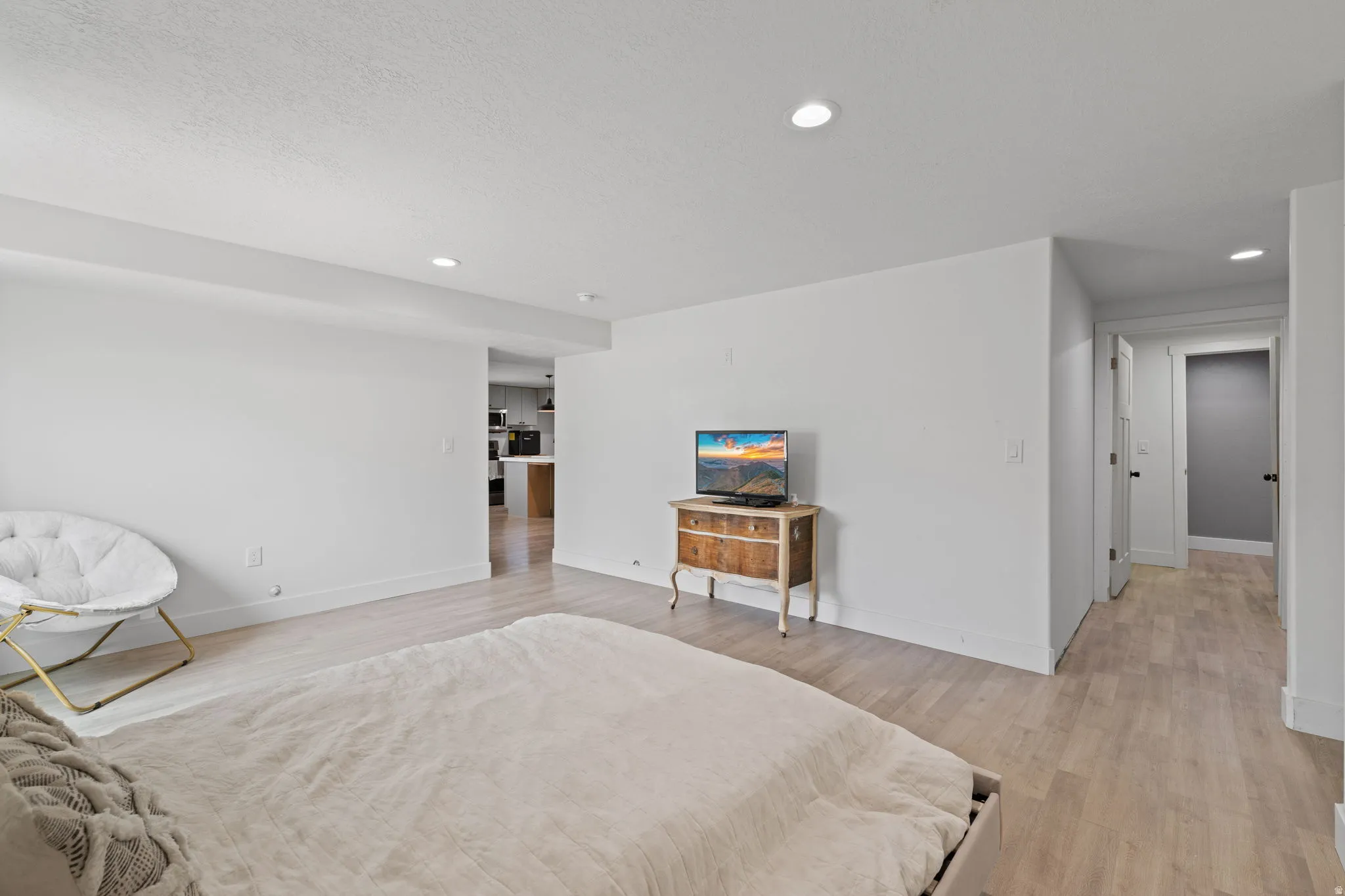 Spacious basement bedroom featuring light wood-finish flooring, recessed lighting, white walls, and white baseboards
