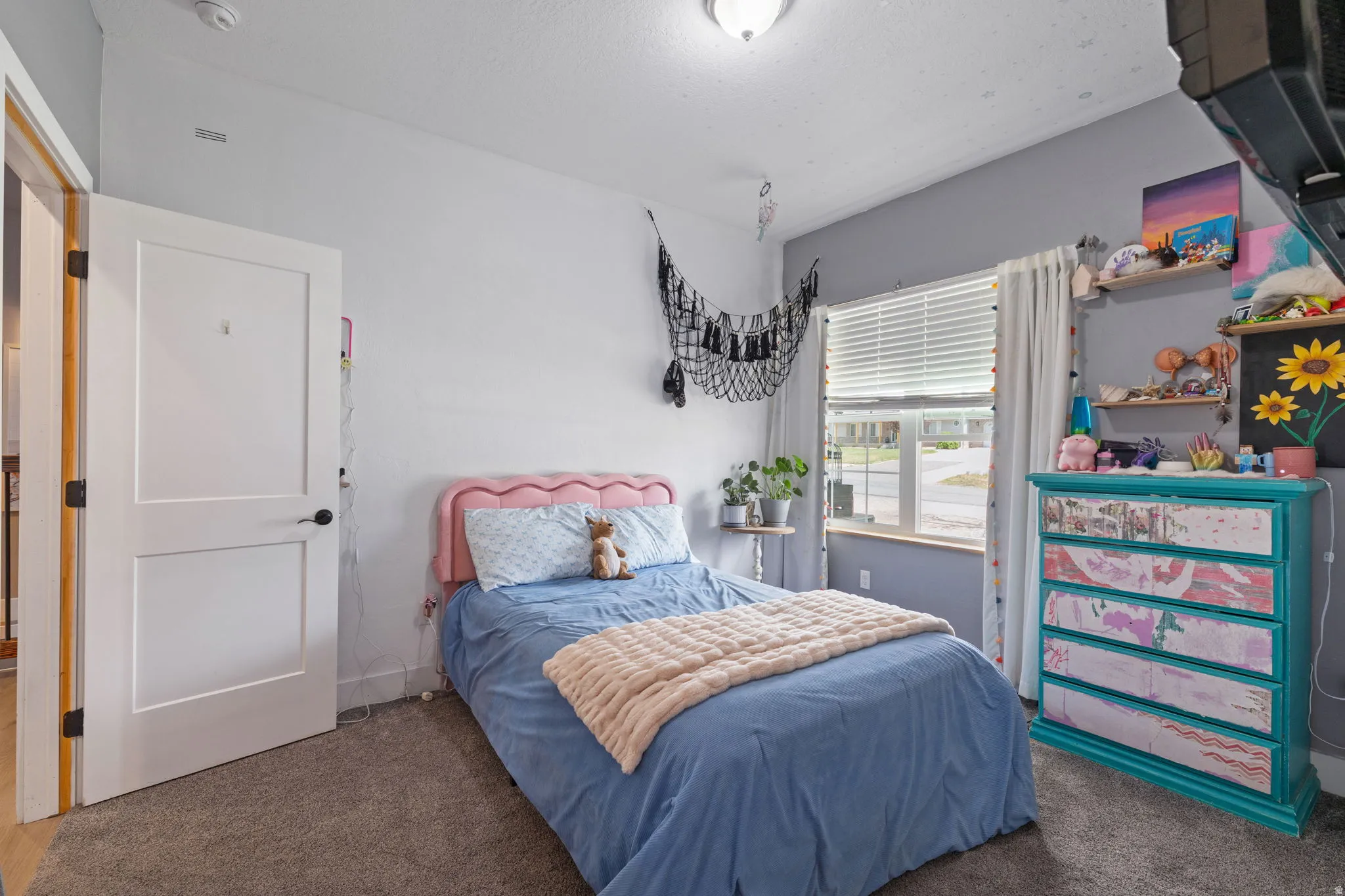 Carpeted room featuring a window with horizontal blinds, a ceiling-mounted light fixture, and a solid core interior door with dark hardware