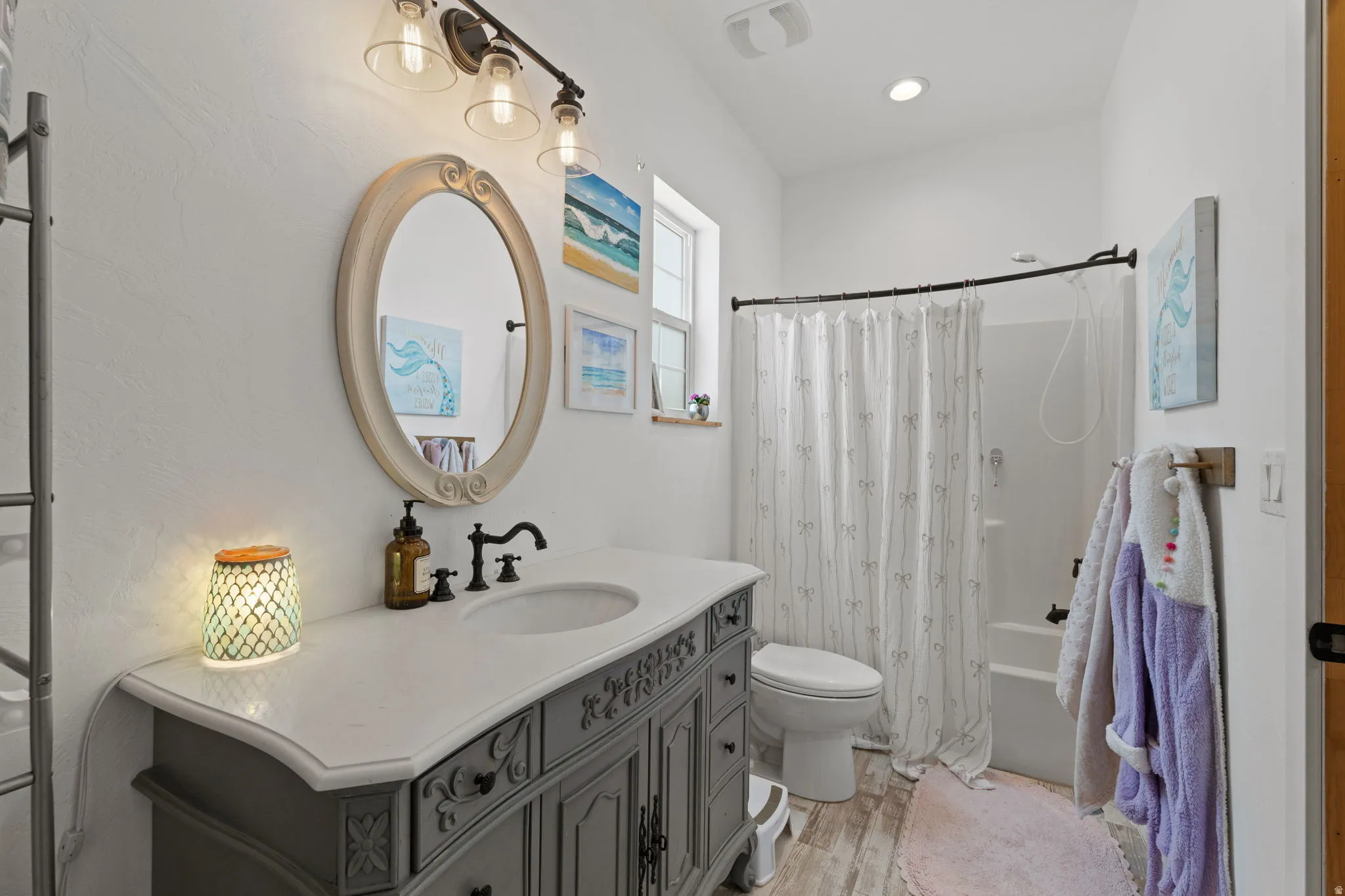 Jack and Jill Bathroom featuring a gray vanity with an integrated sink, an oval framed mirror, and a shower-over-tub combination with a curved rod