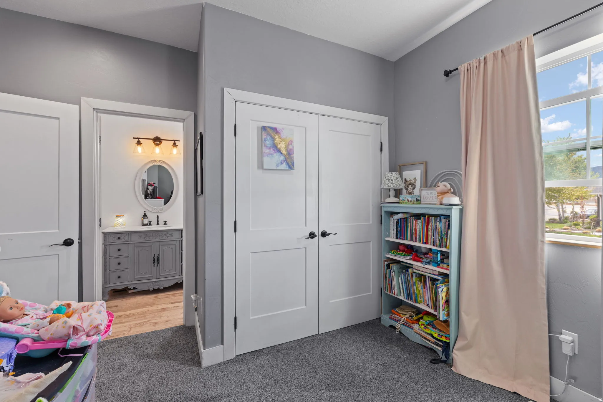Room featuring gray wall paint, gray carpet flooring, a window with white trim, and two white bi-fold closet doors