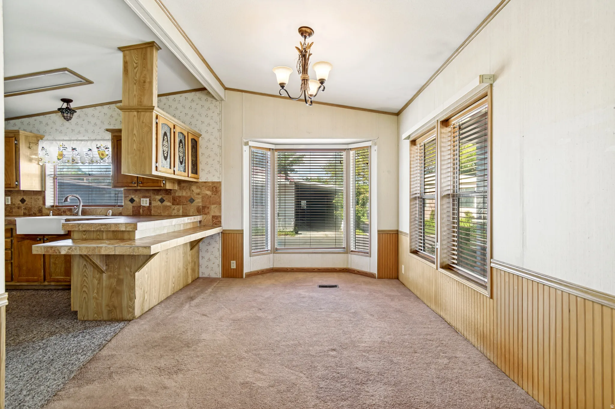 Unfurnished dining area with lofted ceiling, wainscoting, crown molding, carpet, and hanging lights