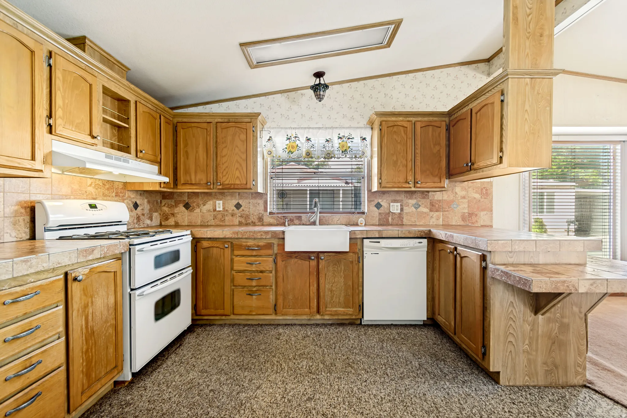 Kitchen with lofted ceiling, a peninsula, white appliances, decorative backsplash, and wood finish cabinetry