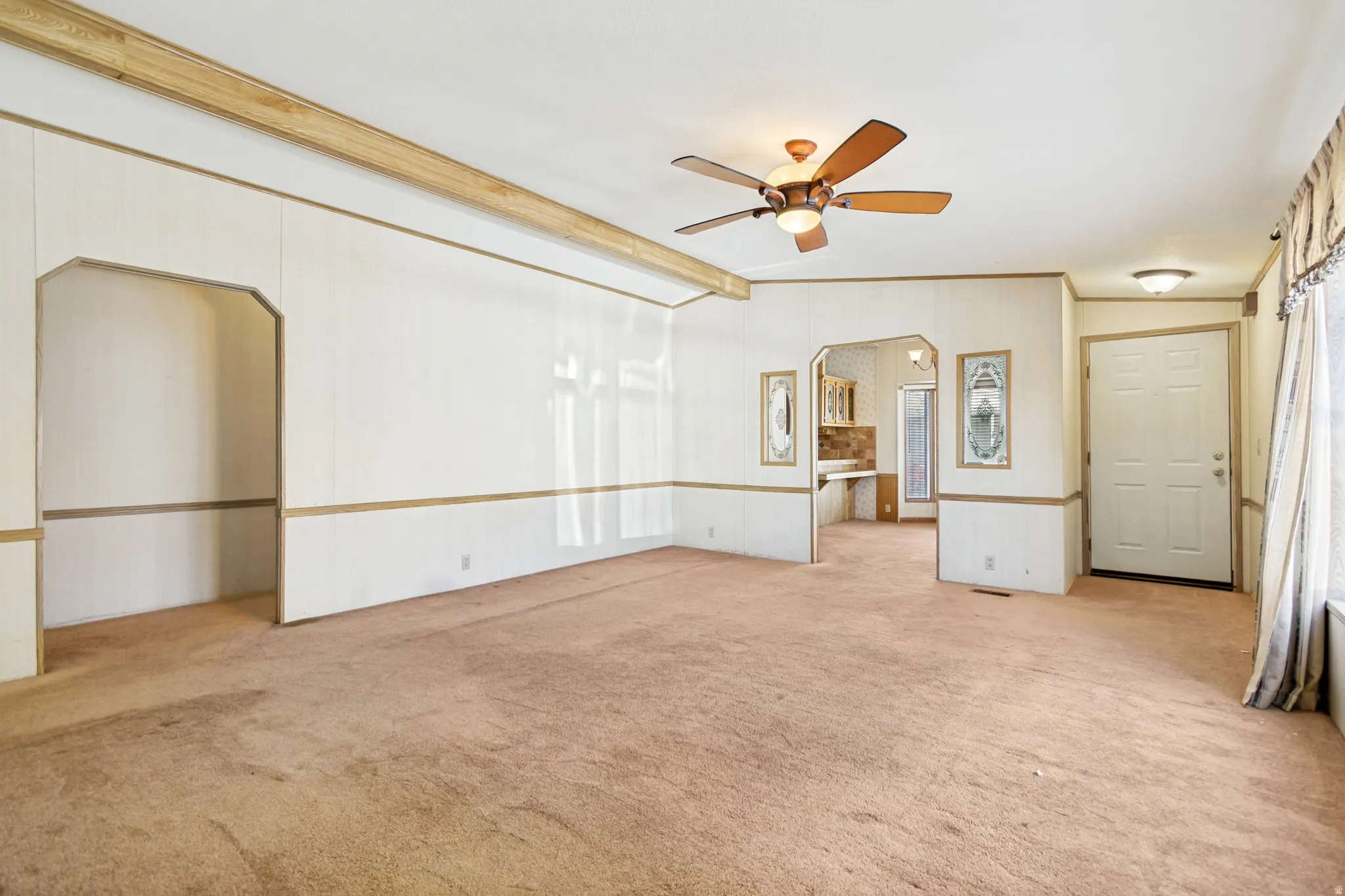 Empty room featuring arched walkways, light carpet, ceiling fan, and vaulted ceiling with beams
