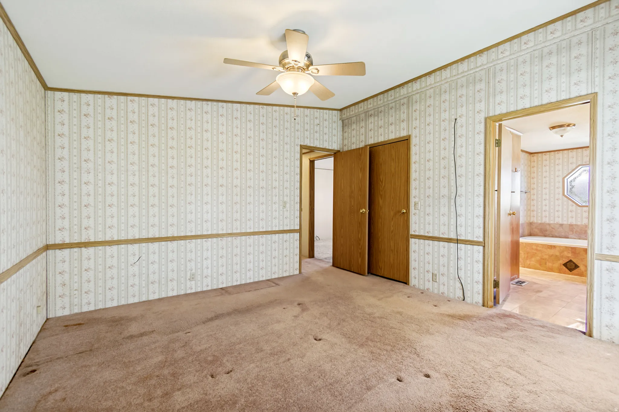 Carpeted spare room featuring ornamental molding, a ceiling fan, and wallpapered walls