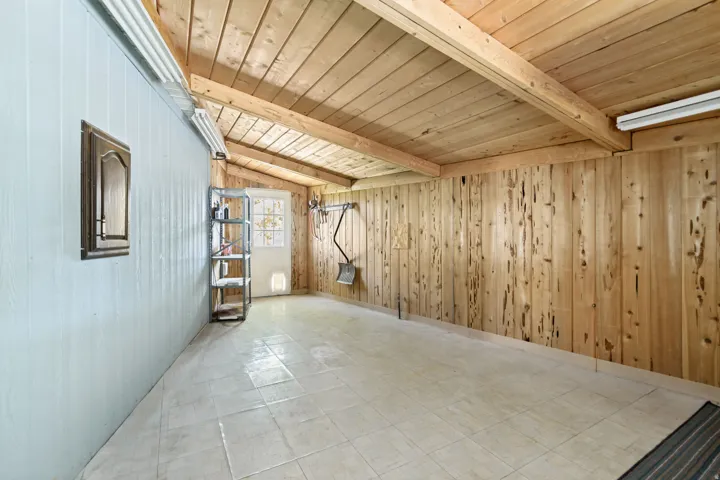 Empty room featuring wooden ceiling, wooden walls, light flooring, and lofted ceiling with beams