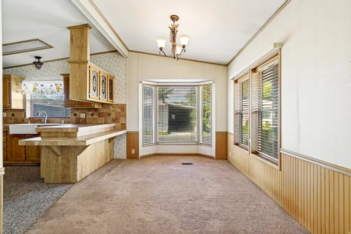 Unfurnished dining area with lofted ceiling, wainscoting, crown molding, carpet, and hanging lights