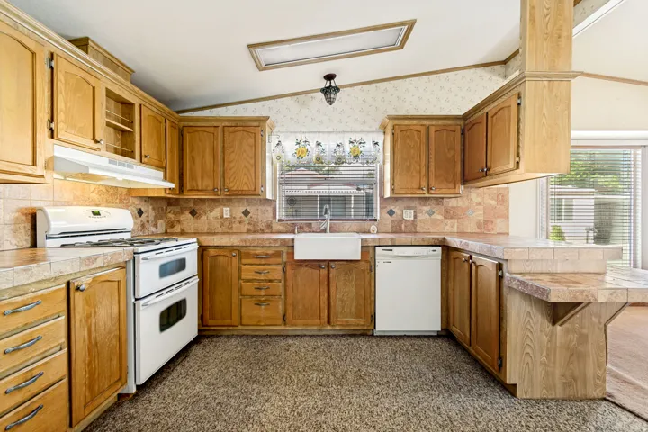 Kitchen with lofted ceiling, a peninsula, white appliances, decorative backsplash, and wood finish cabinetry