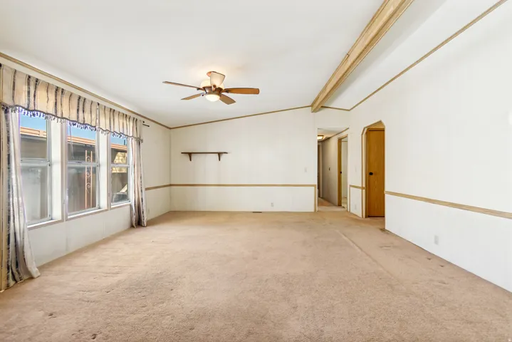 Unfurnished room featuring vaulted ceiling with beams, light colored carpet, and a ceiling fan
