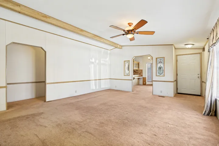 Empty room featuring arched walkways, light carpet, ceiling fan, and vaulted ceiling with beams