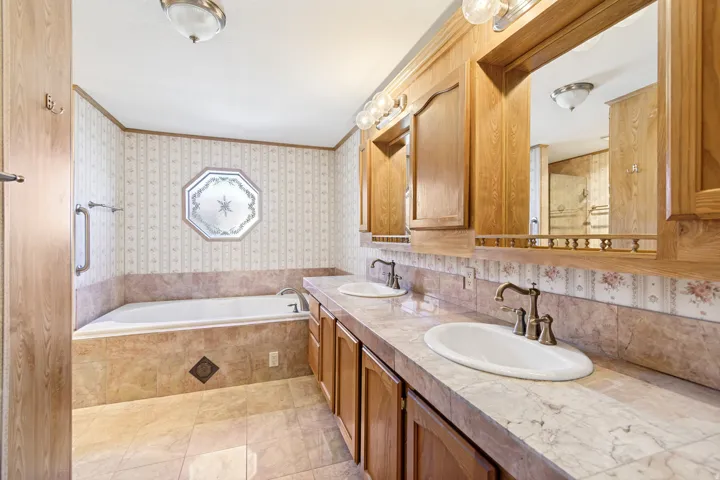 Full bathroom with ornamental molding, wallpapered walls, a bath, and double vanity