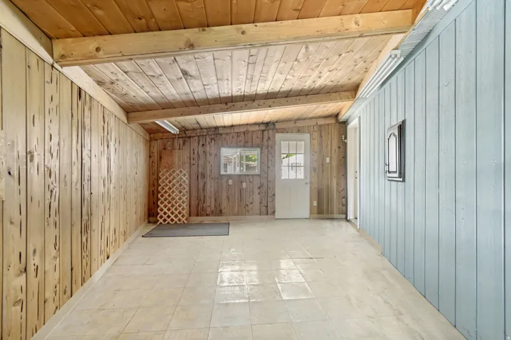 Empty room with wood walls, light floors, wooden ceiling, and lofted ceiling with beams