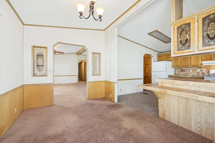 Unfurnished dining area with crown molding, light colored carpet, arched walkways, vaulted ceiling, and wood walls