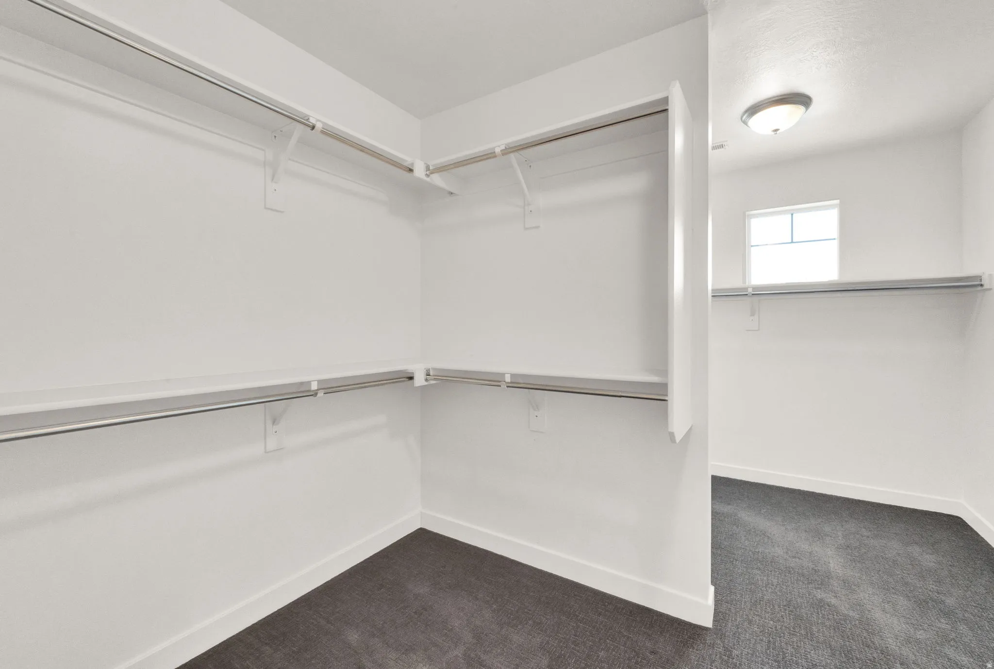 Walk-in closet featuring white walls, dark gray carpeting, and multiple built-in shelving units with hanging rods