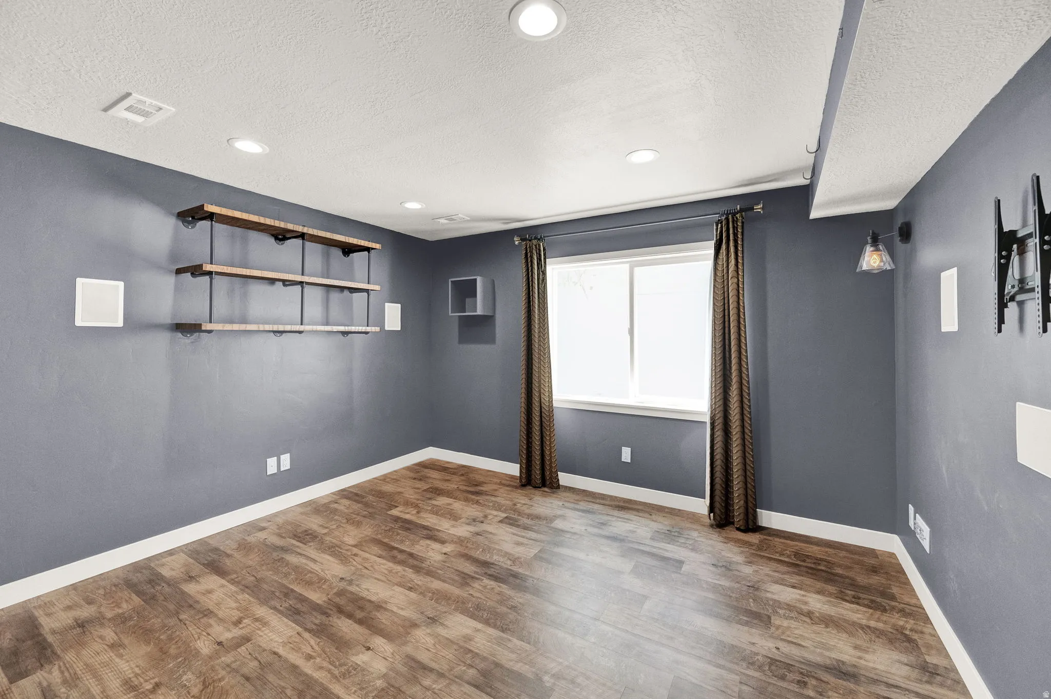 Spacious room featuring wood-finish flooring, recessed ceiling lighting, and a white-trimmed window