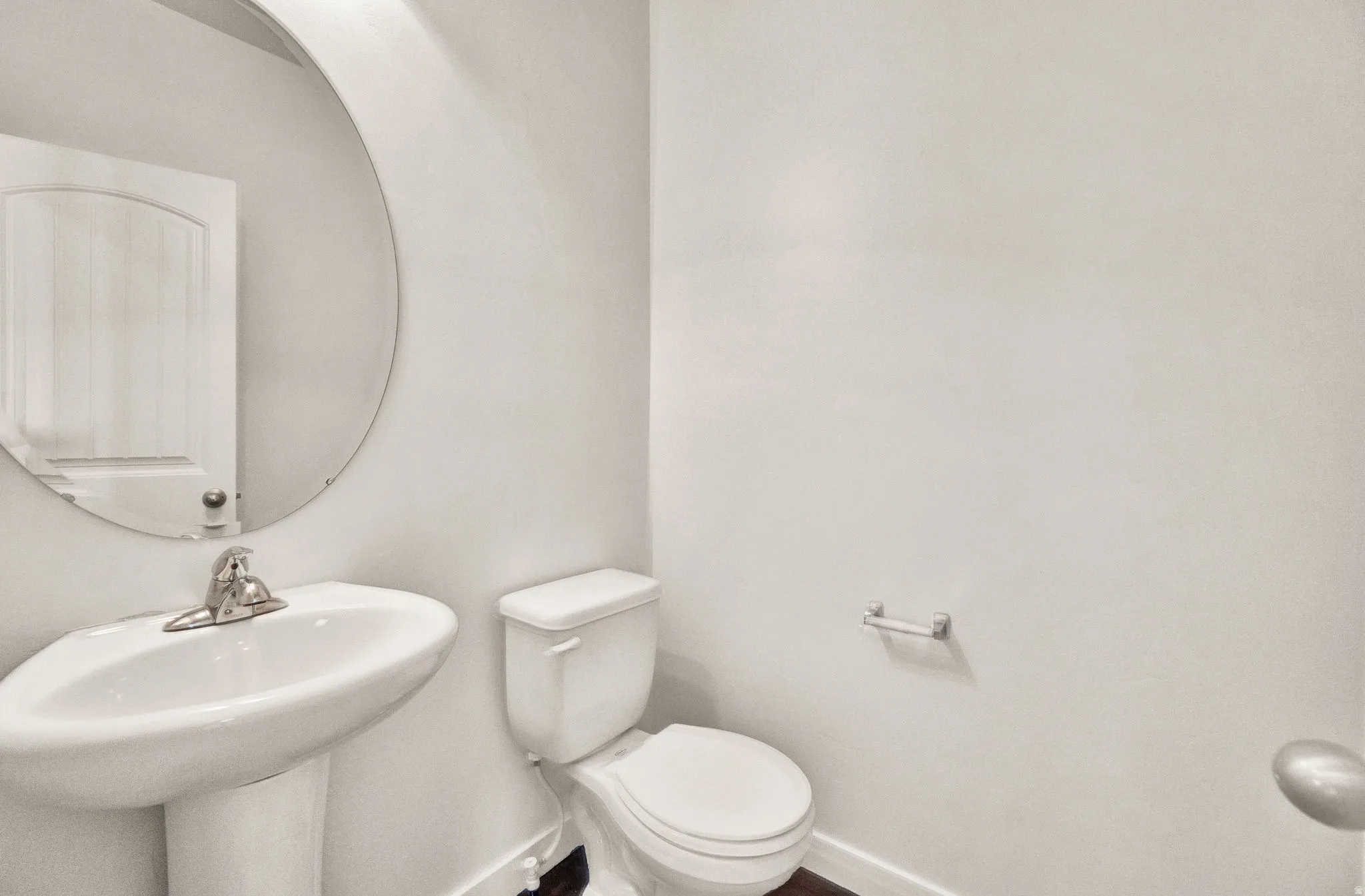 Pedestal sink with chrome faucet, circular wall mirror, and a white toilet