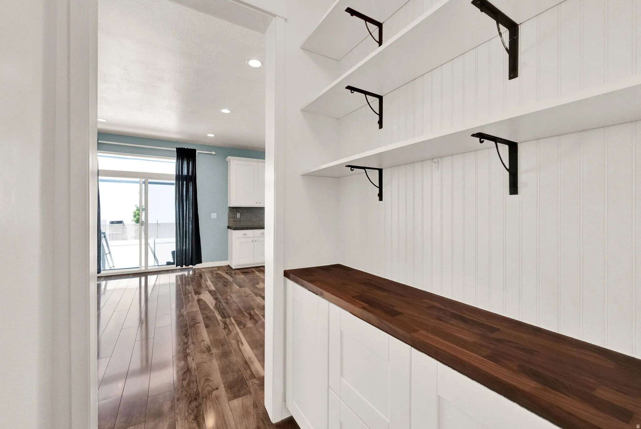 Built-in storage area featuring white beadboard paneling, a rich wood-finish countertop, and three open shelving units with black metal brackets