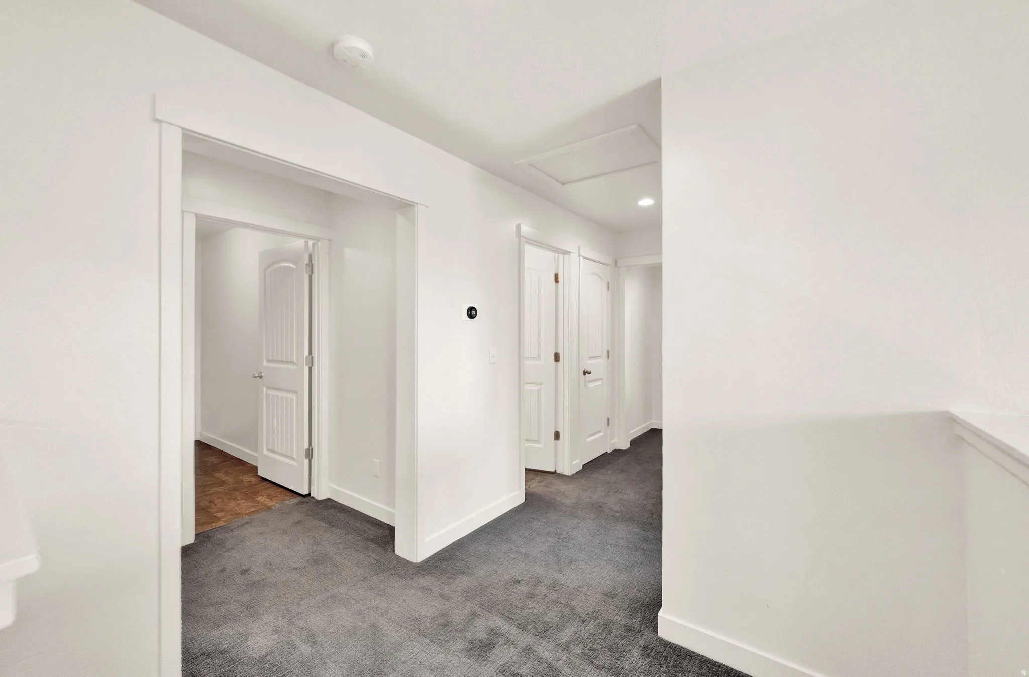 Hallway featuring neutral-toned walls, dark gray carpet, a white framed doorway, and a white interior door with a paneled design
