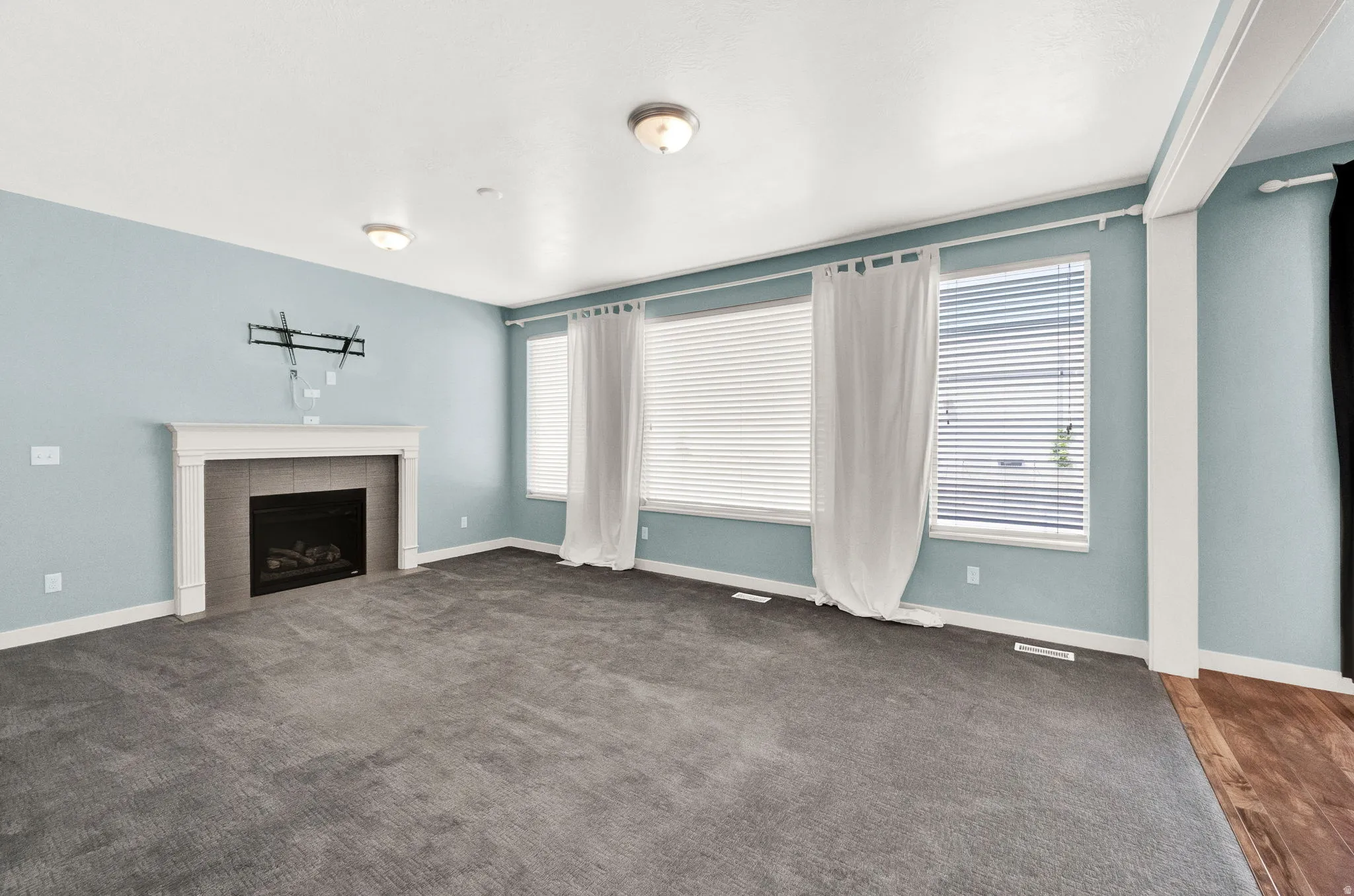 Spacious room featuring a fireplace with a white mantel and gray tile surround, multiple windows with blinds, gray carpeting, and integrated ceiling lighting