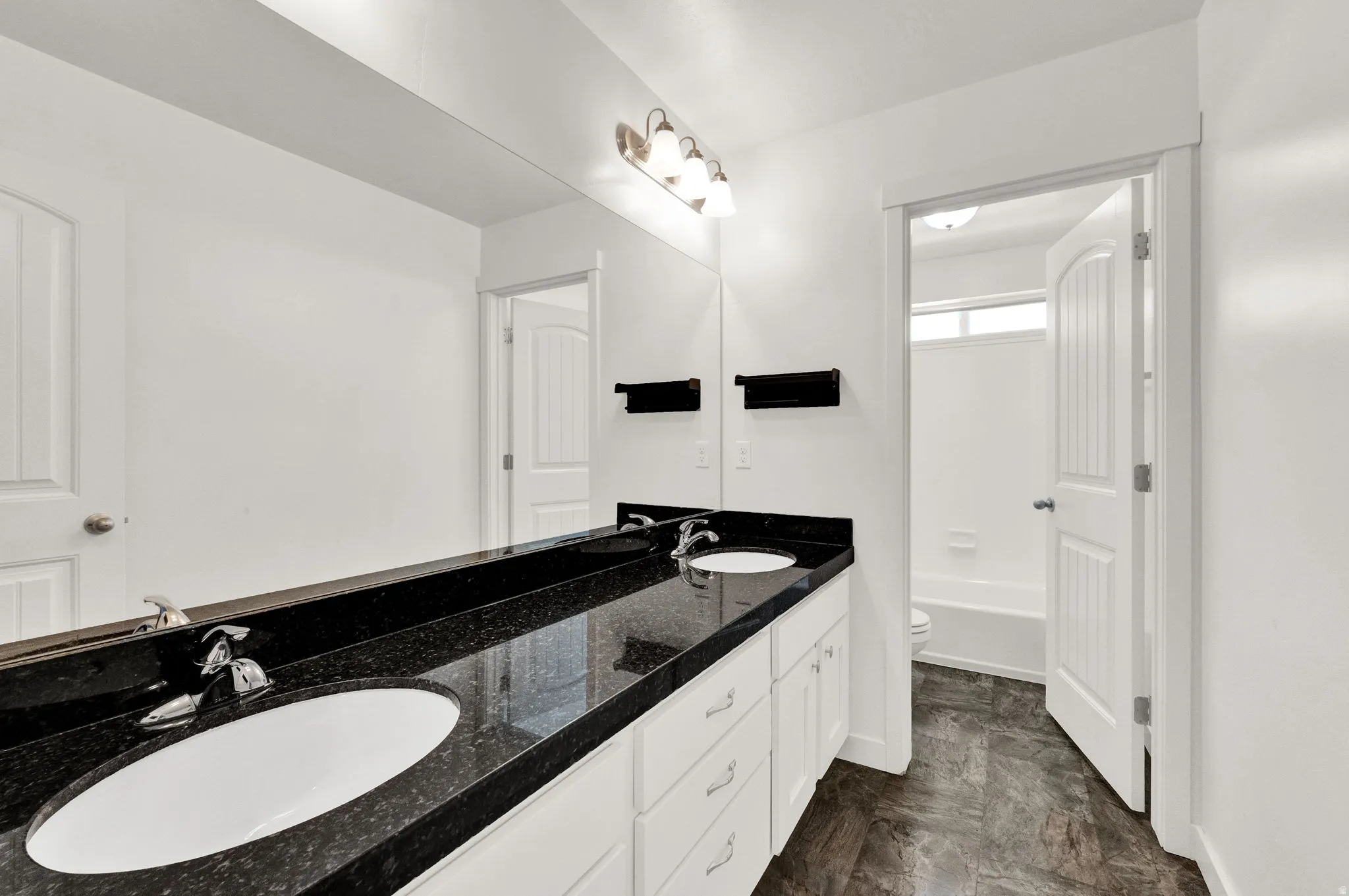 Double vanity featuring a black speckled countertop with two undermount sinks, white cabinetry, and chrome fixtures