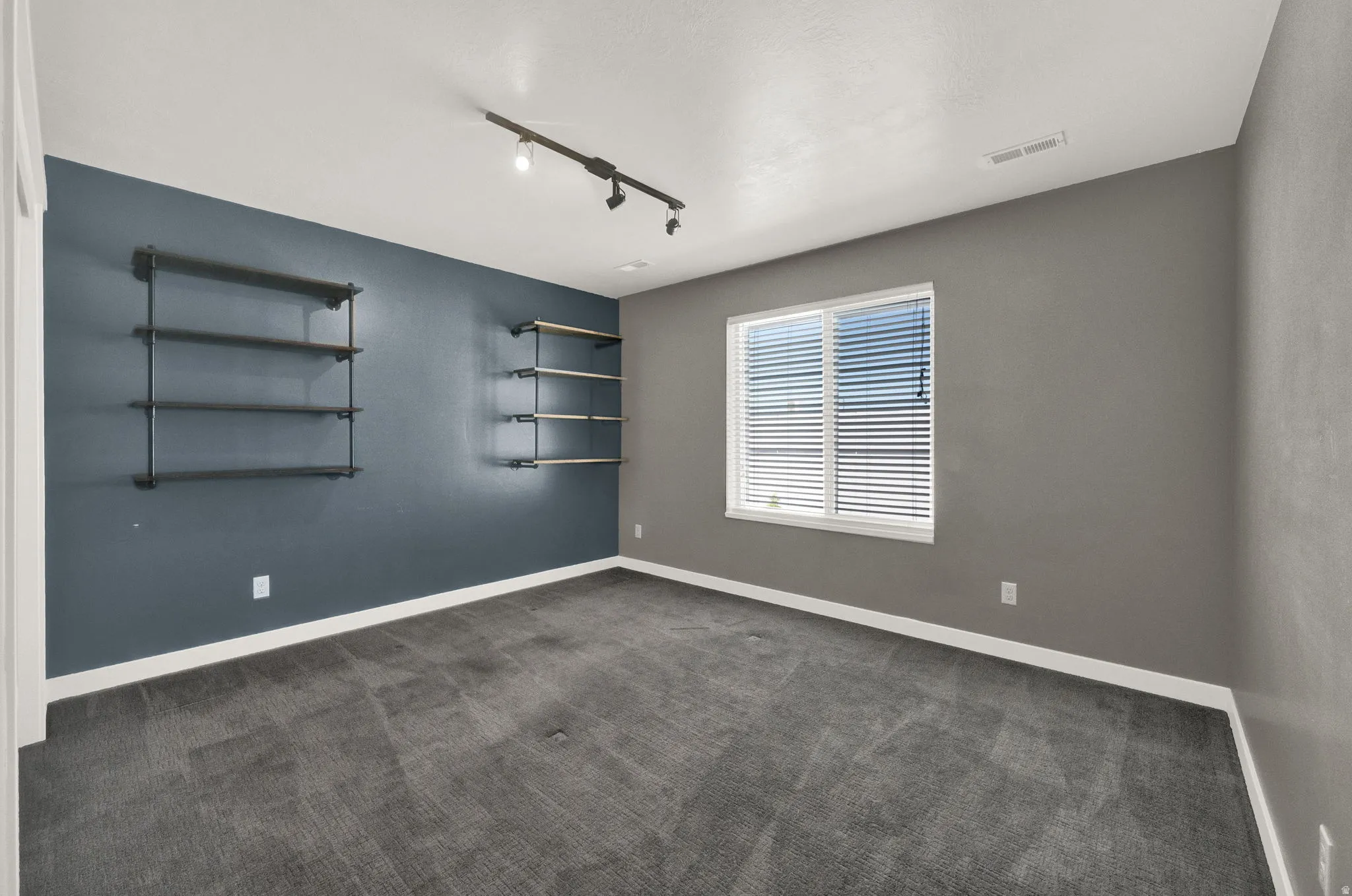 Room featuring industrial-style shelving, track lighting, and a window with white blinds