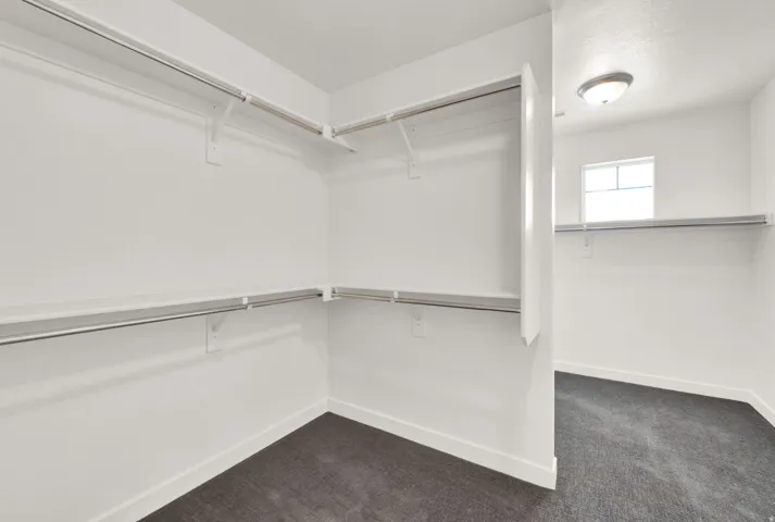 Walk-in closet featuring white walls, dark gray carpeting, and multiple built-in shelving units with hanging rods
