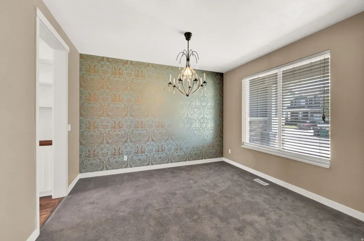 Room featuring a statement wall with patterned wallpaper, grey carpet, and a decorative chandelier