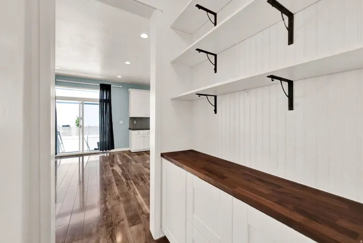 Built-in storage area featuring white beadboard paneling, a rich wood-finish countertop, and three open shelving units with black metal brackets
