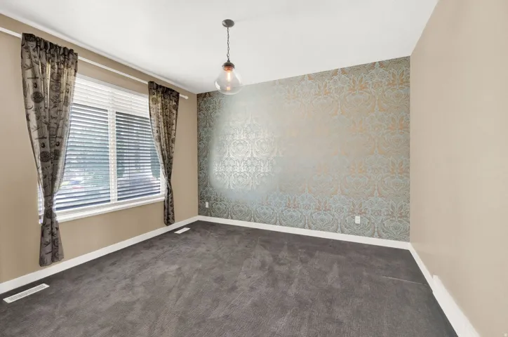 Neutral-toned room featuring a large window with blinds, patterned accent wall, recessed lighting, and carpeted flooring