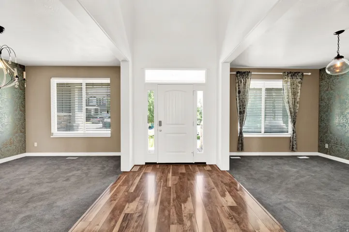 Entry foyer with wood-finish flooring, flanked by carpeted areas featuring windows with blinds