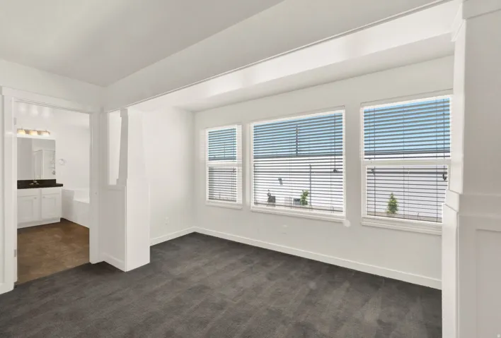 Spacious room with dark gray carpeting and three windows featuring horizontal blinds