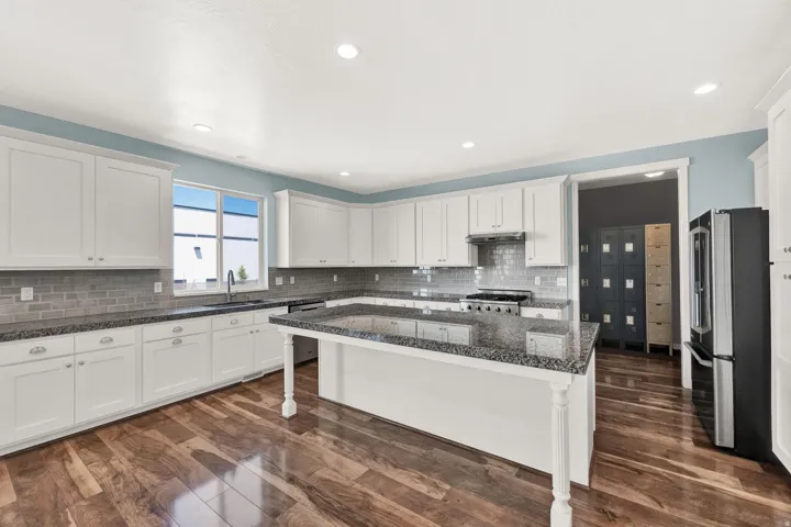 Spacious kitchen featuring white cabinetry, dark stone countertops, a subway tile backsplash, a stainless steel range, and wood-finish flooring