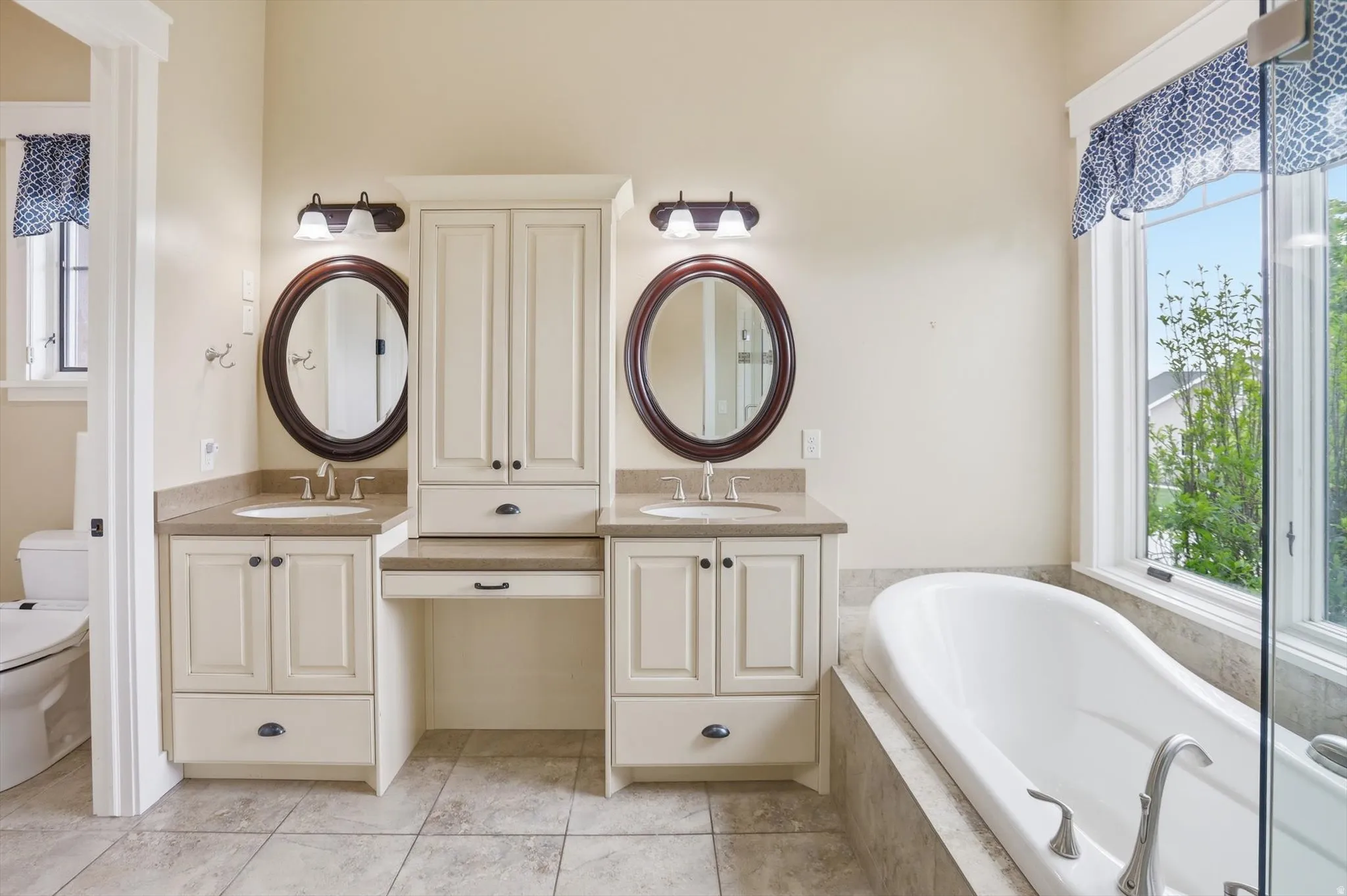 Dual vanity with light cabinetry and oval mirrors, featuring a built-in storage tower and a separate makeup counter