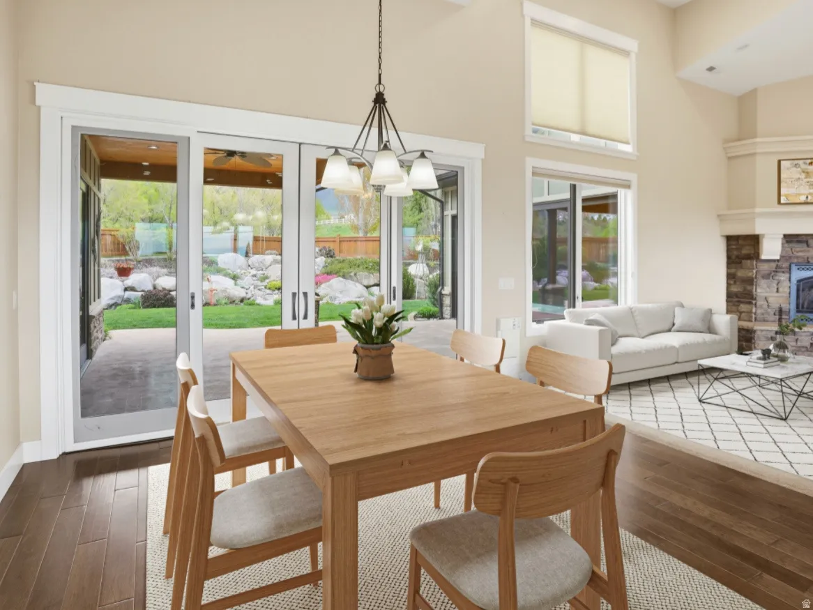 Open-concept living space featuring wood-finish flooring, a stone-faced fireplace, a vaulted ceiling, and sliding glass doors opening to an outdoor patio
