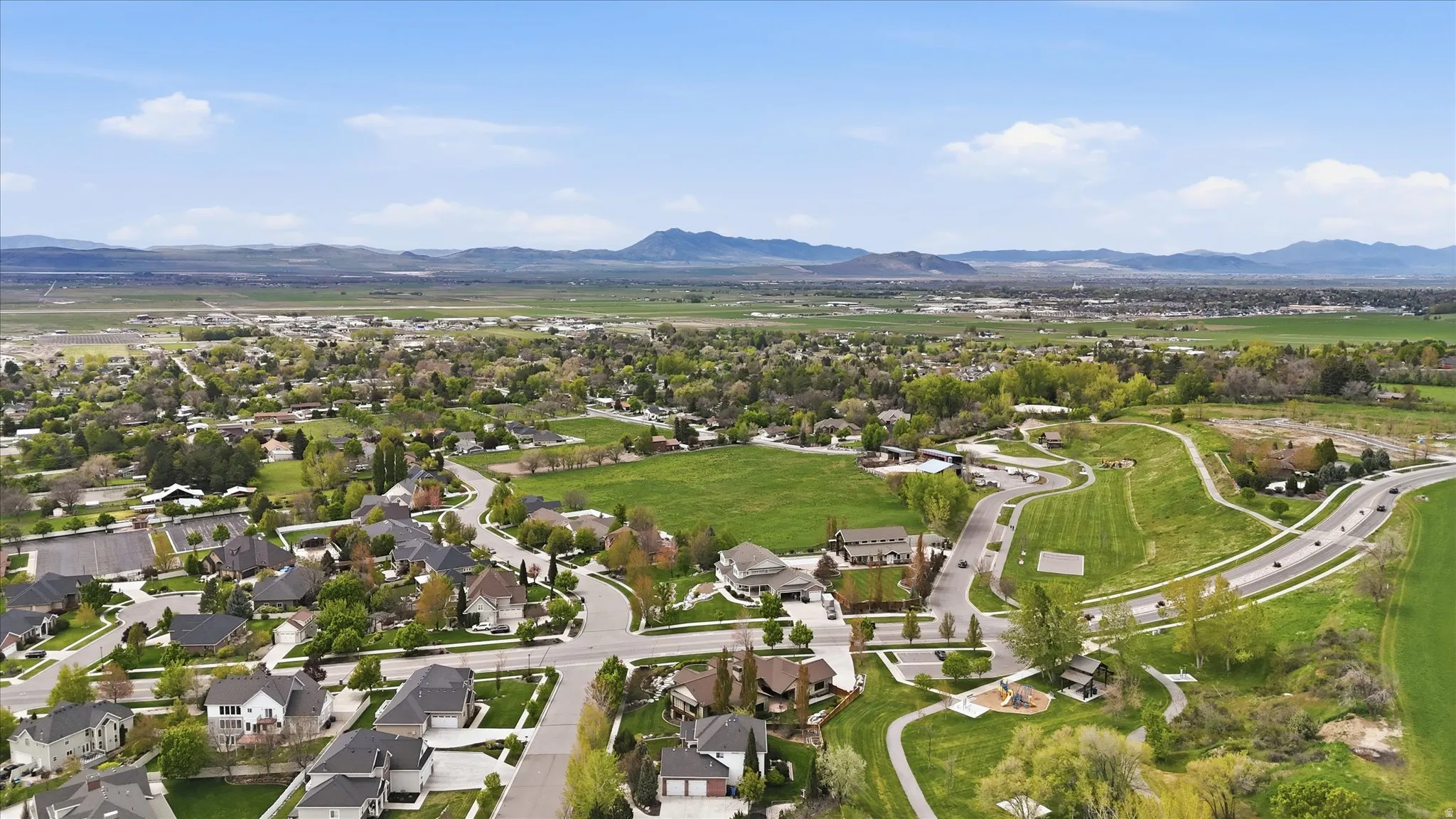Expansive aerial perspective showcasing a residential development with surrounding green spaces and distant mountainous terrain