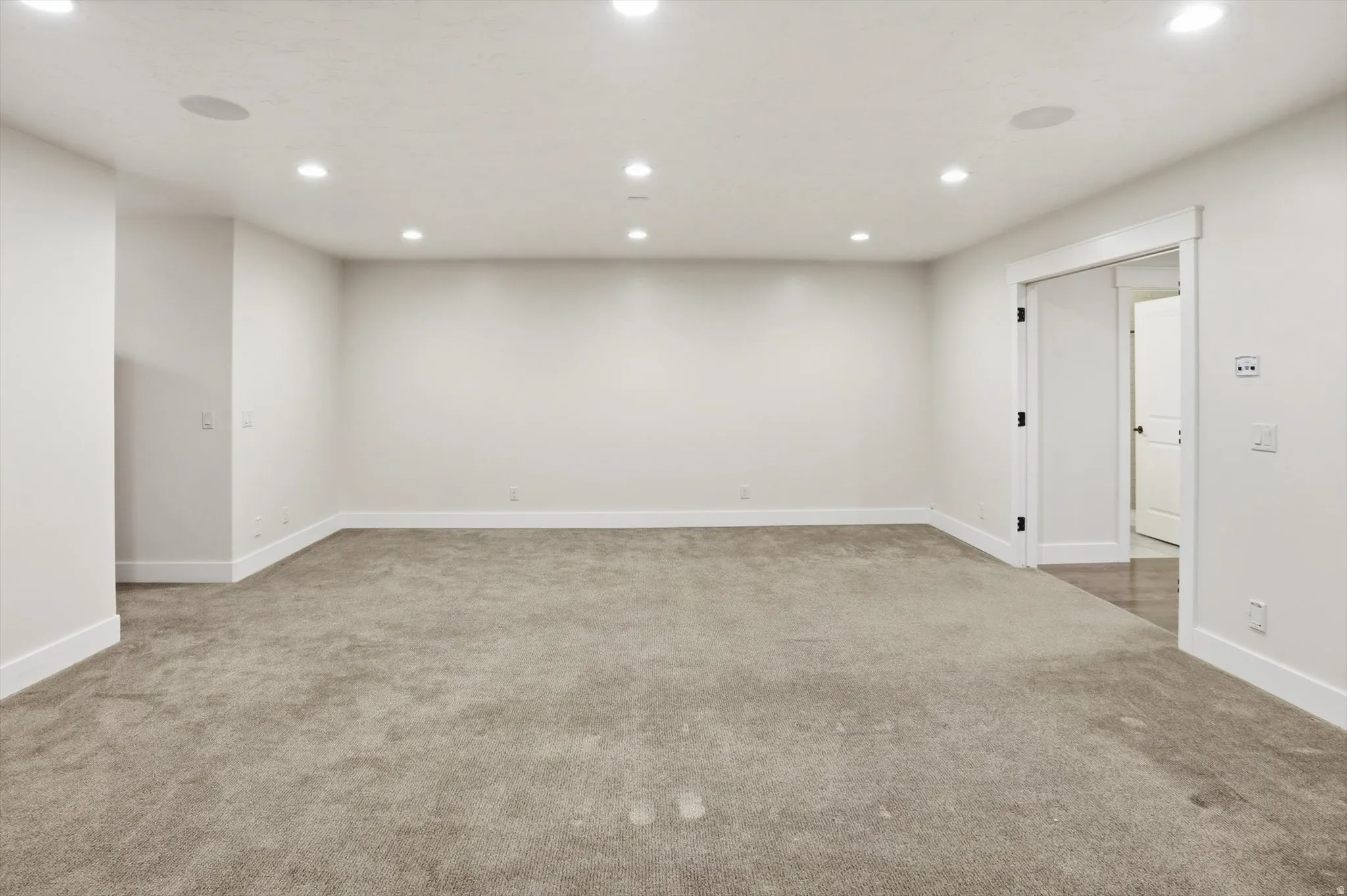 Spacious room featuring neutral carpeting, white walls, recessed ceiling lighting, and white baseboards