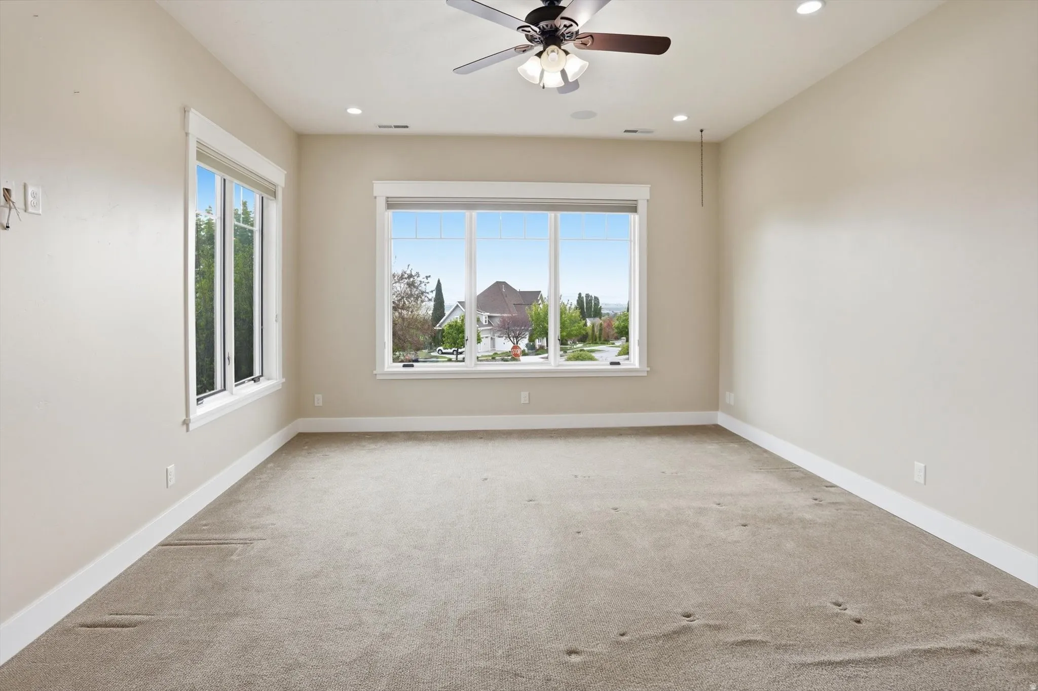 Spacious room featuring multiple large windows, recessed lighting, a ceiling fan fixture, neutral wall tones, and white trim throughout