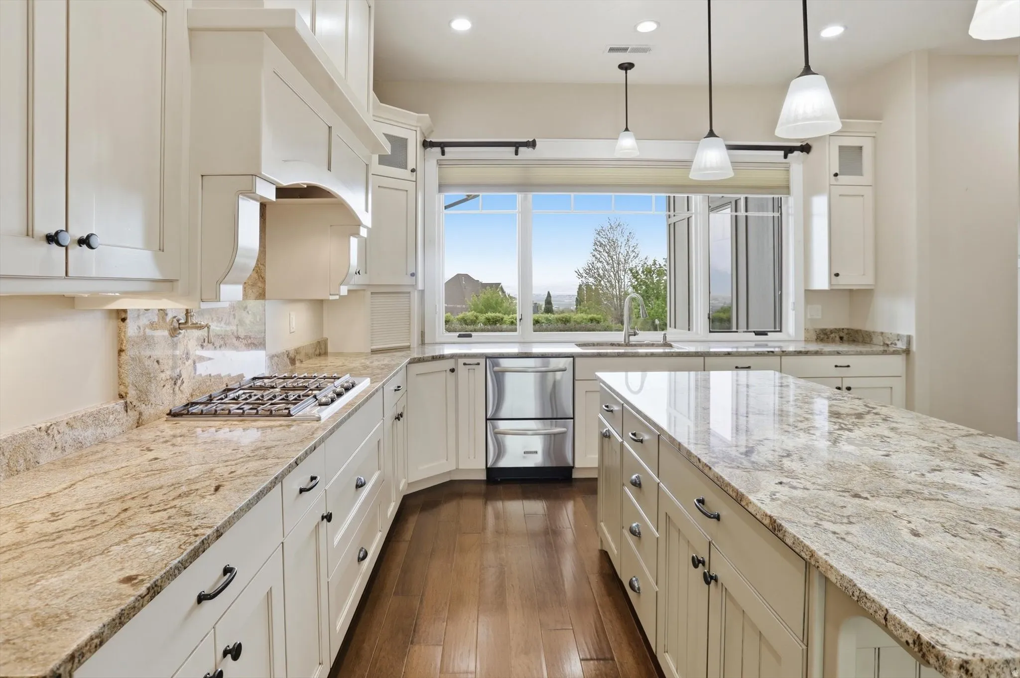 Spacious kitchen featuring extensive stone countertops, custom cabinetry with dark hardware, a built-in gas range, stainless steel appliances, and wood-finish flooring