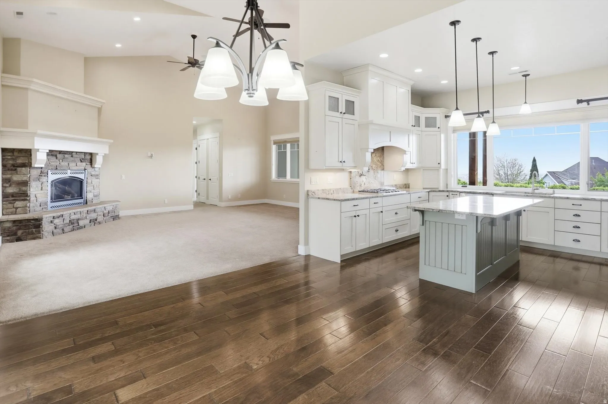 Expansive open-concept kitchen featuring white cabinetry, a central island with pendant lighting, and large windows
