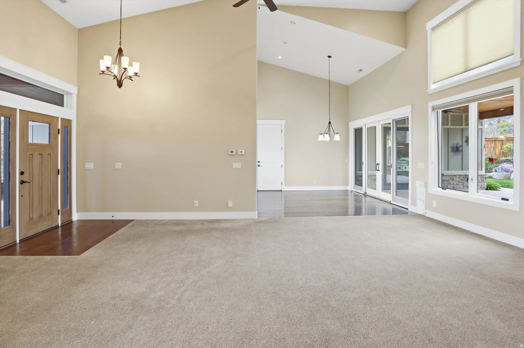 Vaulted ceilings in an open-concept living area with light-toned carpet and a wood-finish entryway