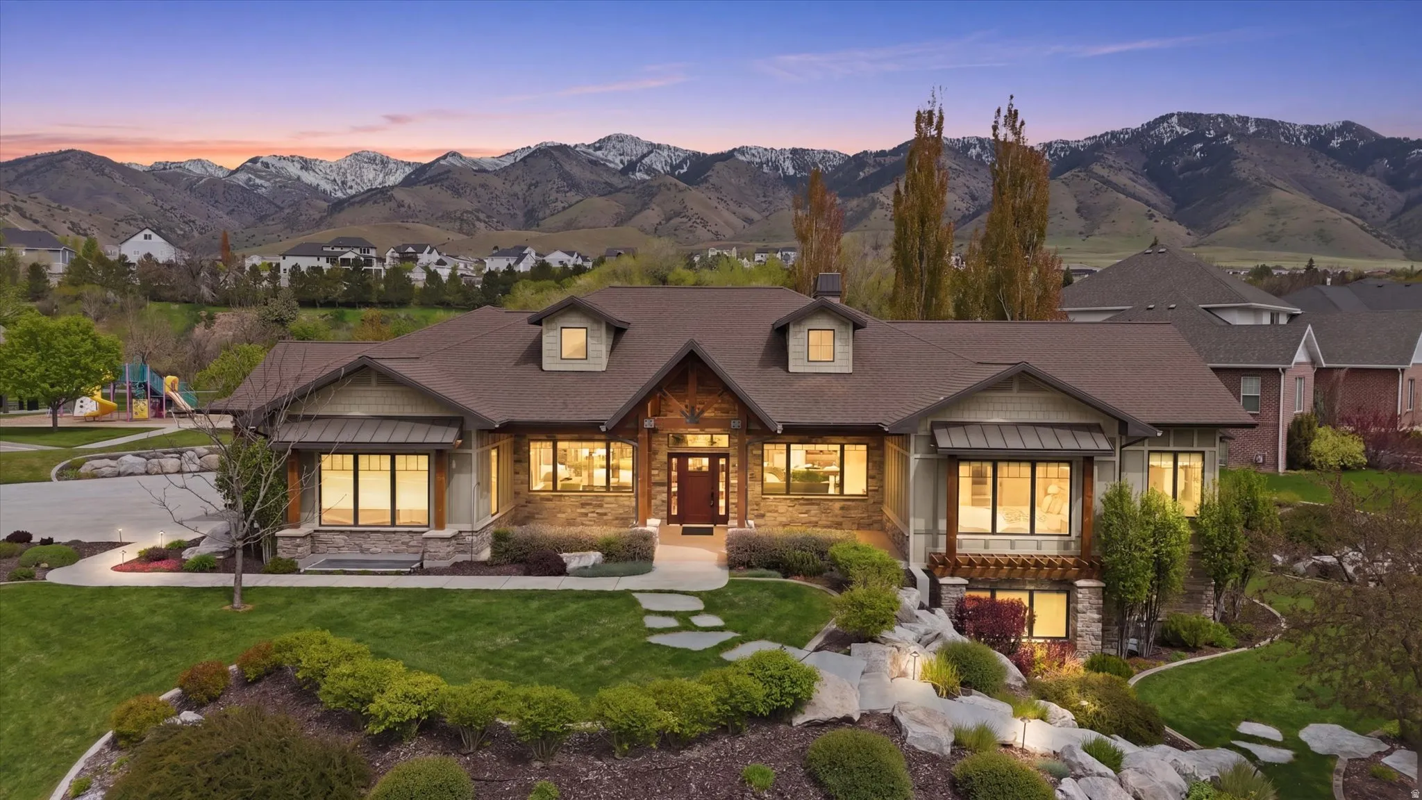 Craftsman-style home featuring a stone and wood facade, a prominent front entry with a warm wood door, multiple gabled dormers, and a meticulously landscaped front yard with stepping stones