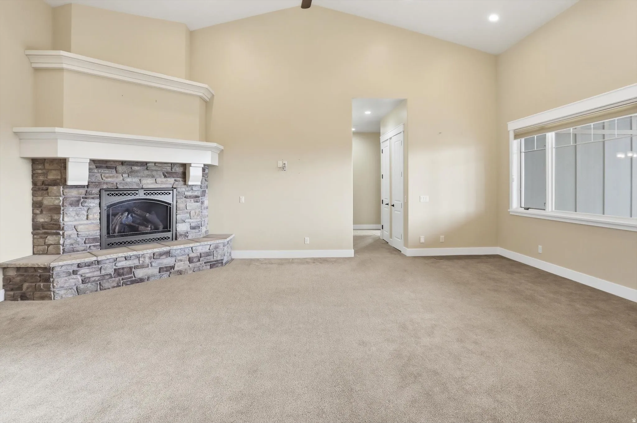 Spacious room featuring a stone fireplace with a white mantel, vaulted ceilings, recessed lighting, and large windows with integrated blinds