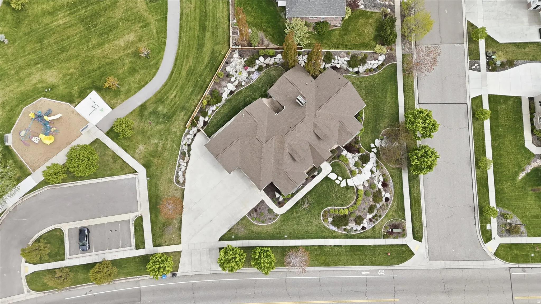 Brown shingle roofline, expansive concrete driveway, and rock landscaping