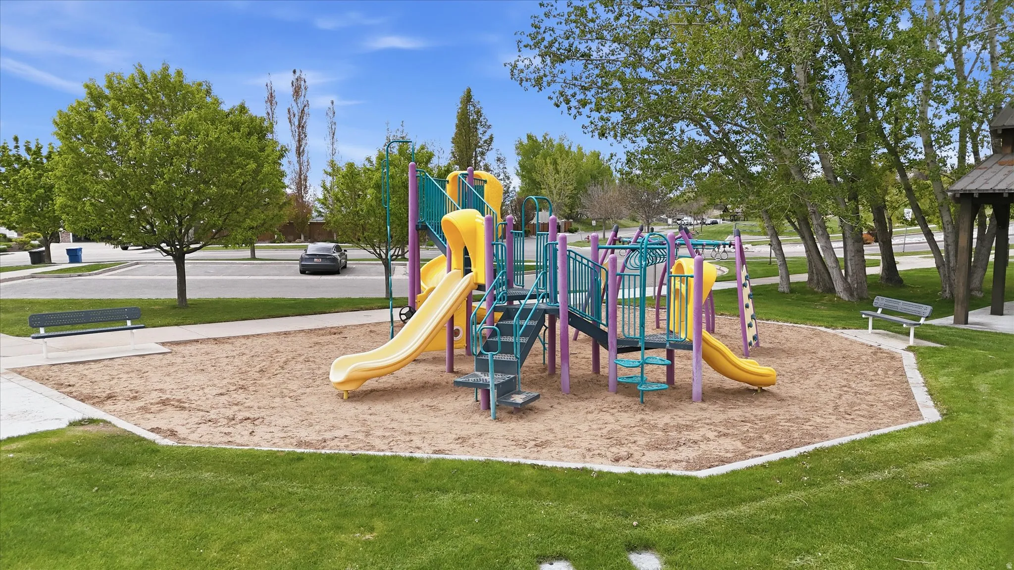 Community park featuring a large children's play structure with slides and climbing elements, a sand-covered play area, and surrounding green lawn