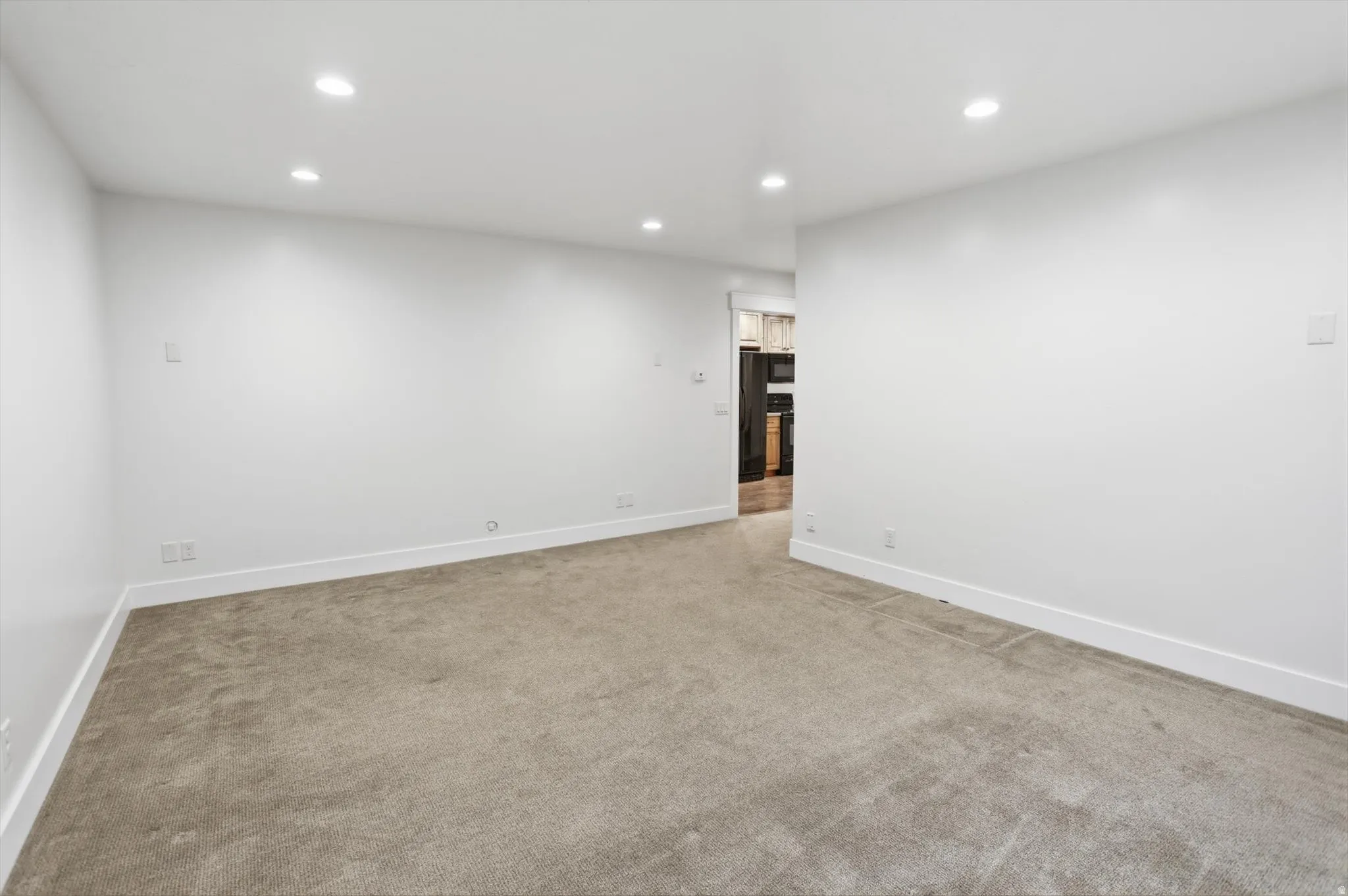 Expansive room featuring plush carpeting, recessed ceiling lighting, crisp white walls, and a wide entryway