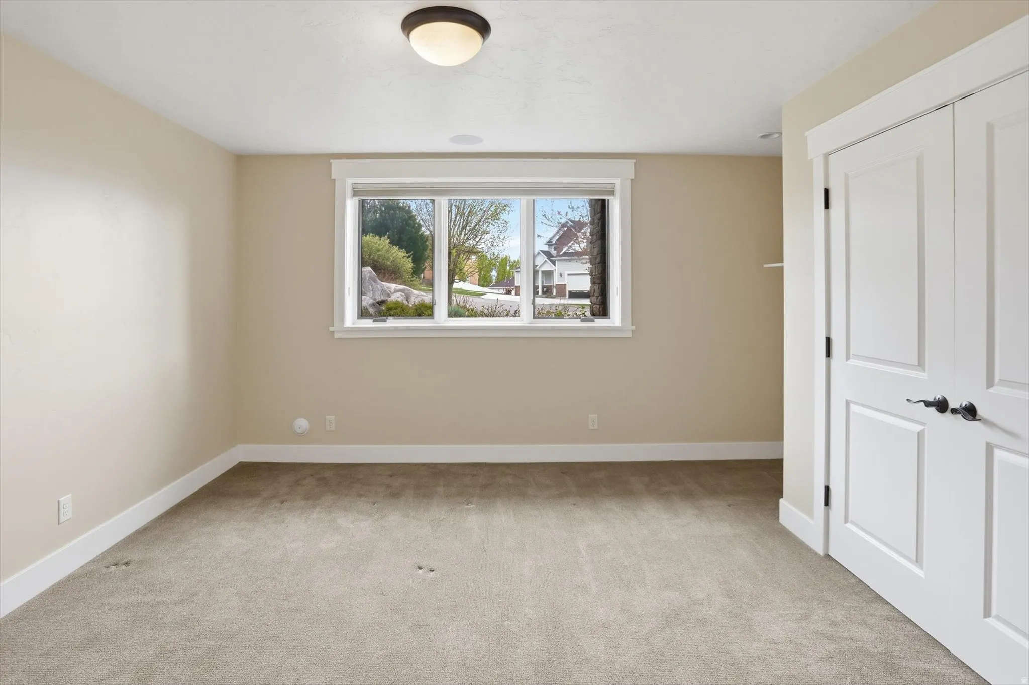 Spacious room featuring neutral carpeting, a large three-panel window with white trim, and a ceiling-mounted light fixture