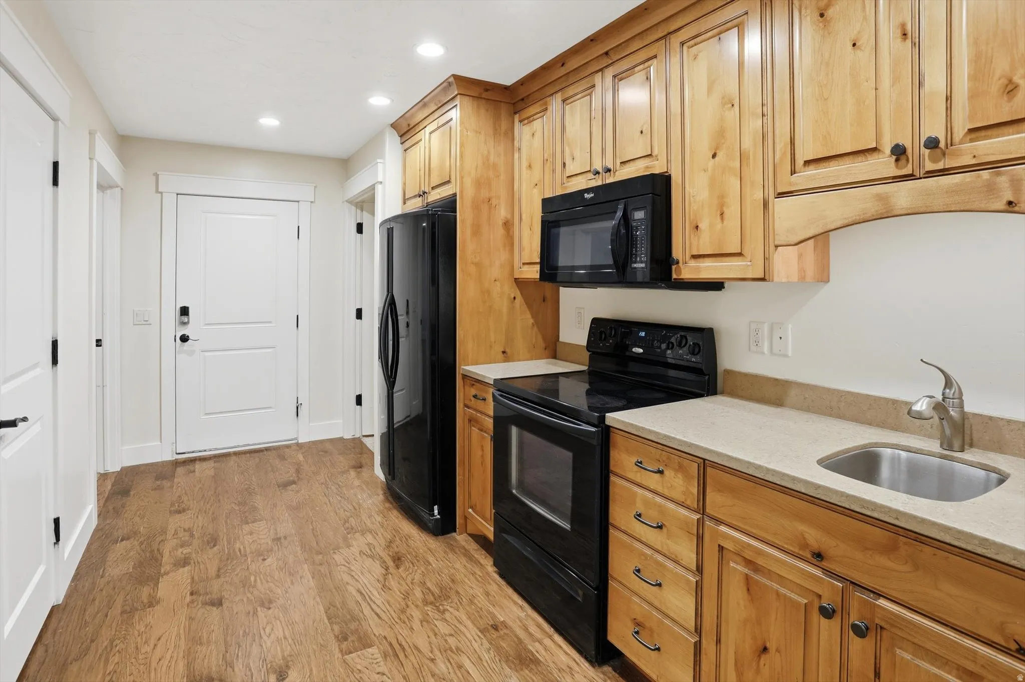 Kitchenette featuring natural wood cabinetry, black appliances, a stainless steel sink, and wood-finish flooring
