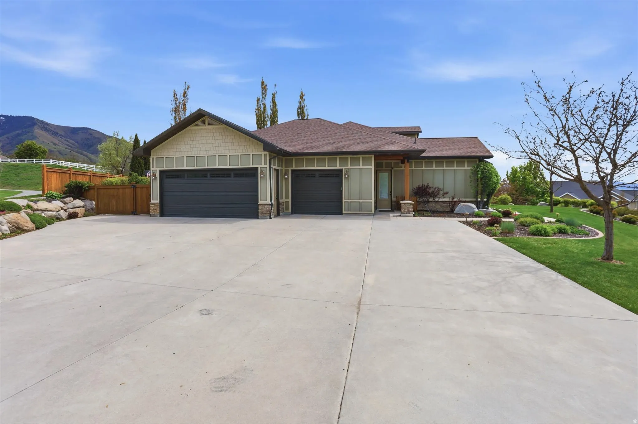 Ranch-style residence featuring a broad concrete driveway, a two-car garage with dark doors, and light green siding with shingle accents