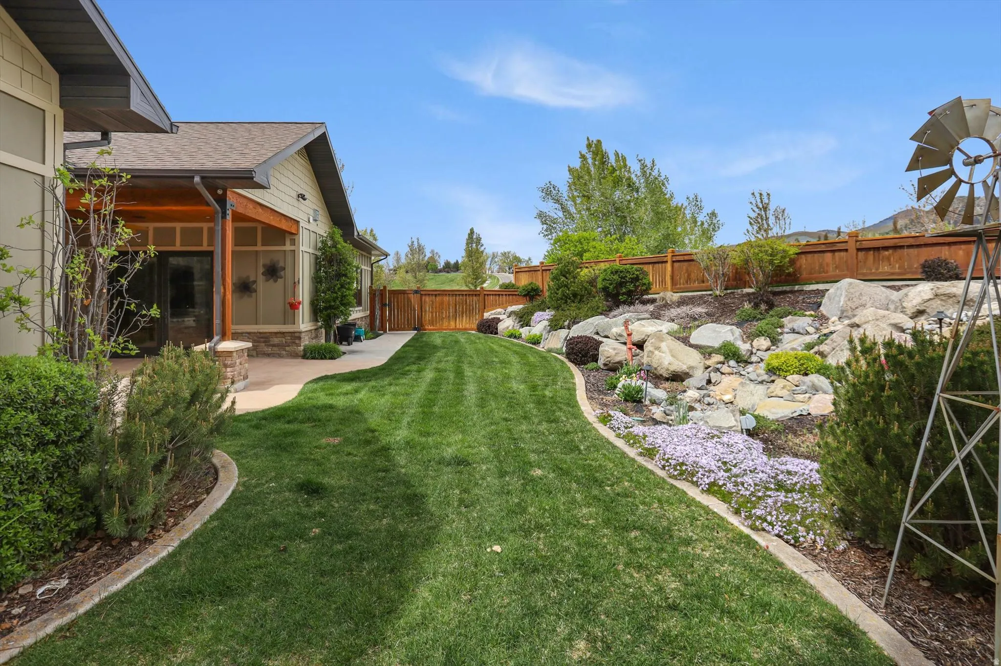Expansive backyard featuring a manicured lawn, a rock garden with various plantings, and a wooden privacy fence