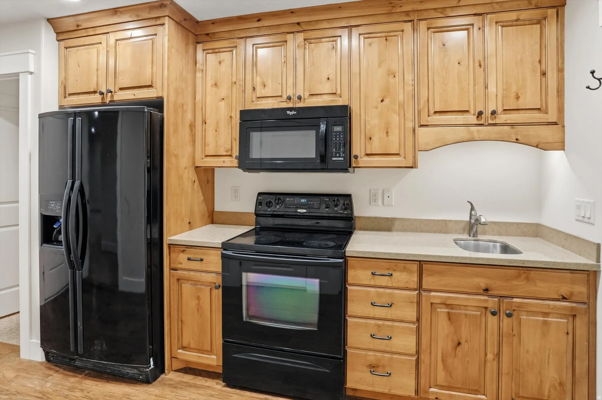 Compact kitchen featuring light wood cabinetry, black appliances, a stainless steel sink, light-toned countertops, and recessed lighting