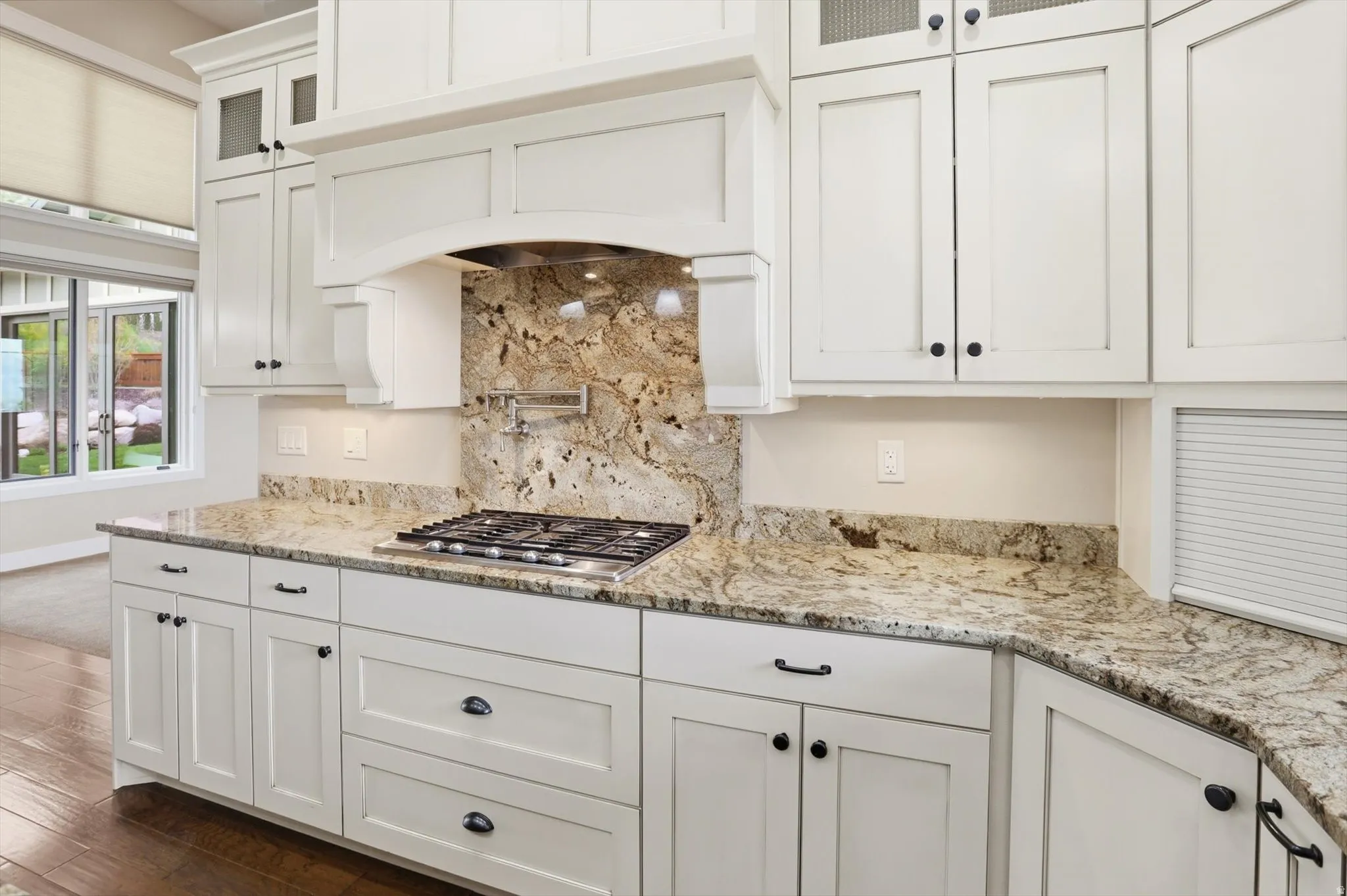 Kitchen featuring a gas range, a pot filler faucet, stone countertops, a full-height stone backsplash, and white shaker-style cabinetry with black hardware